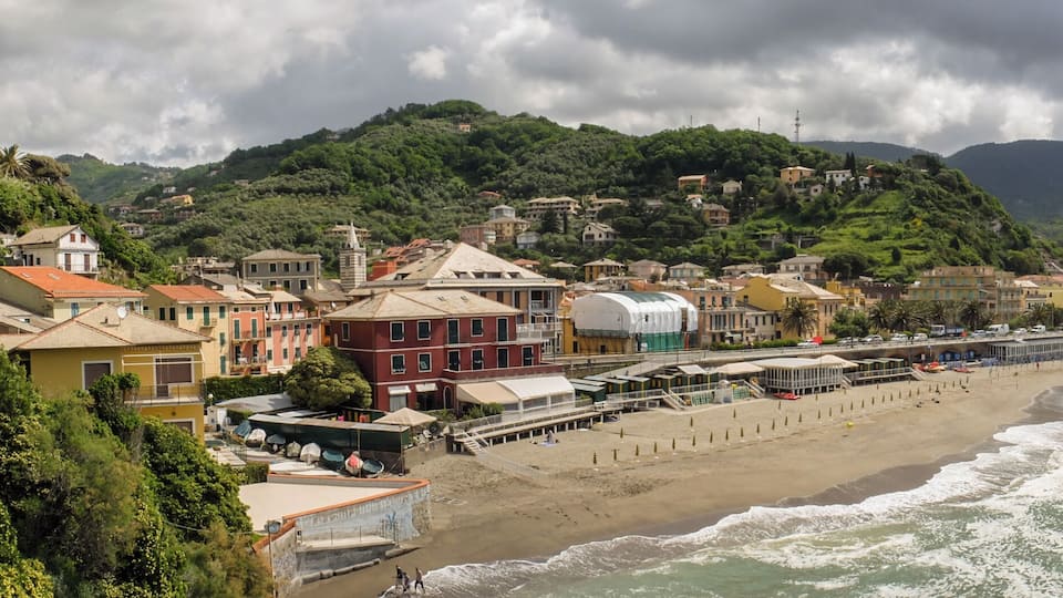 A coastal town with a beach, buildings, and mountains in the background.
