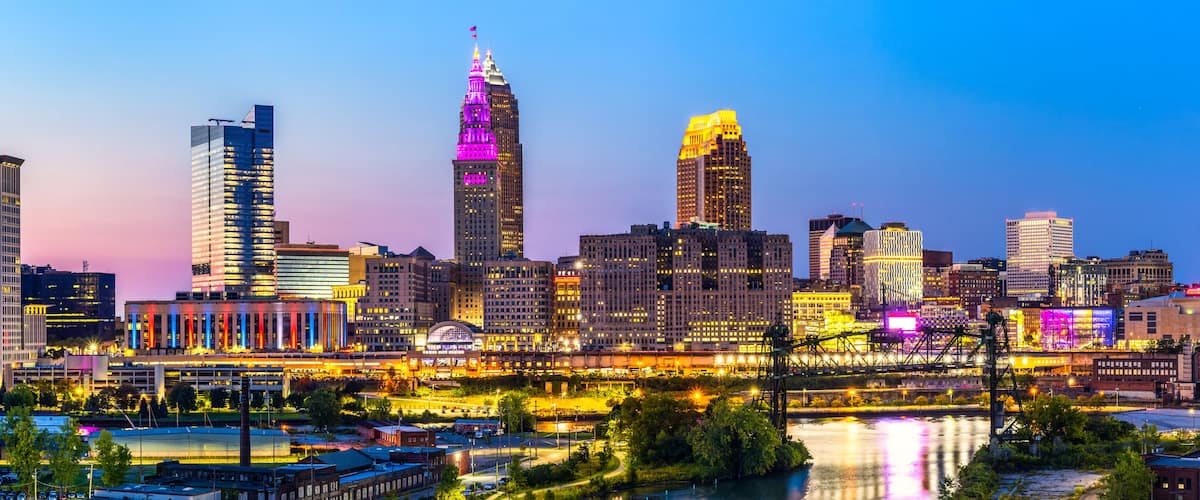 A city skyline with illuminated buildings and a river in the foreground.