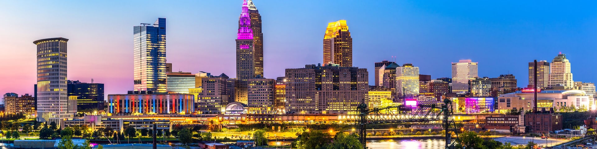 A city skyline with illuminated buildings and a river in the foreground.