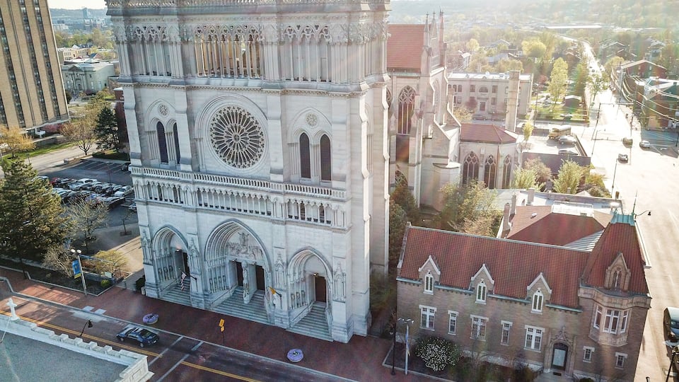 A large cathedral with intricate architecture, a prominent rose window, and a smaller adjacent building with a red roof.