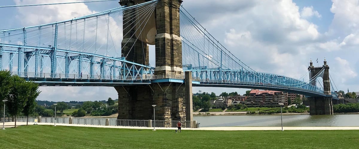 Un puente colgante grande con dos torres, un río abajo y una zona verde al frente.