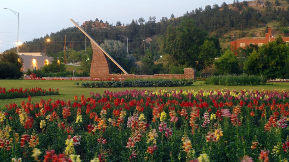A field of colorful flowers, a brick structure, and a hill with trees in the background.
