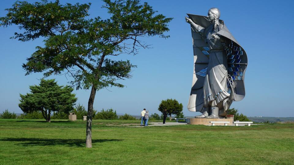 A statue in a grassy field with trees and a clear sky.