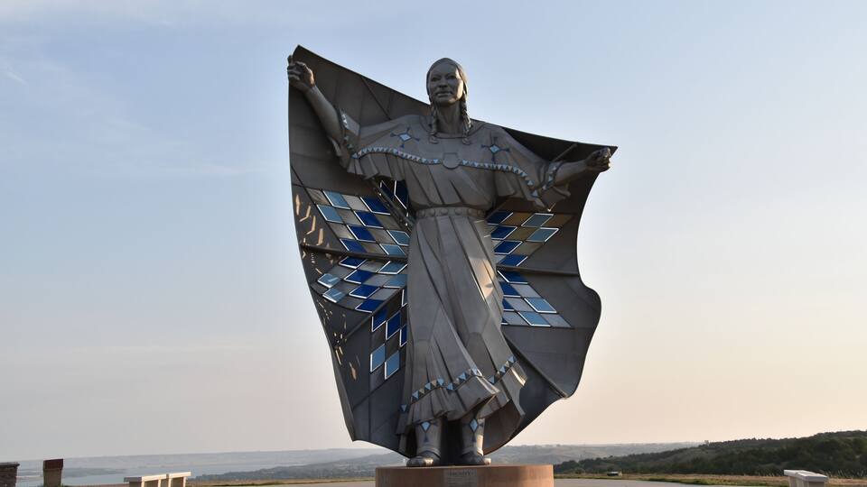 A large statue with a wide-open cape, set against a clear sky.