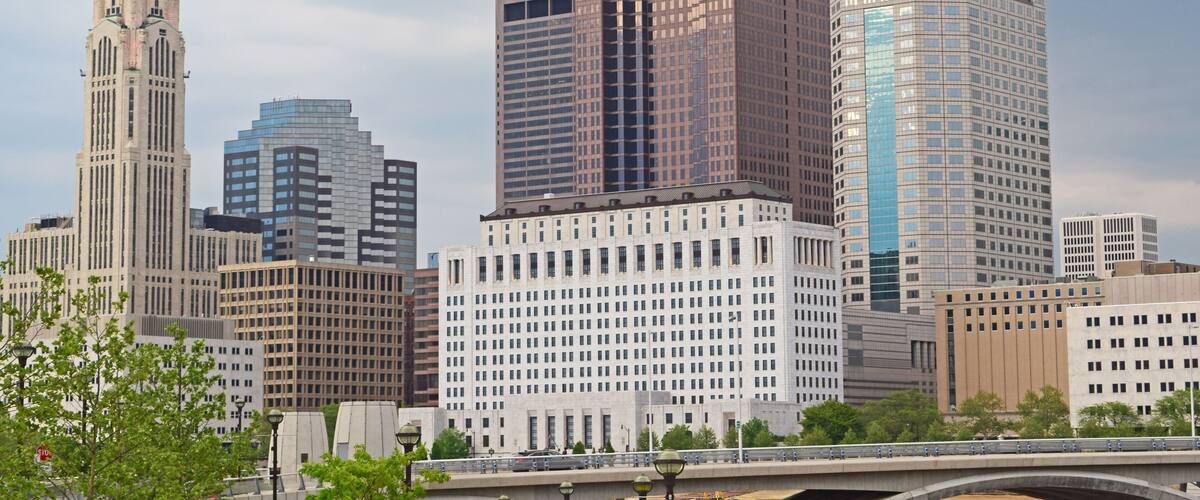 A city skyline with a mix of modern and historic buildings, including a prominent tower and a bridge in the foreground.