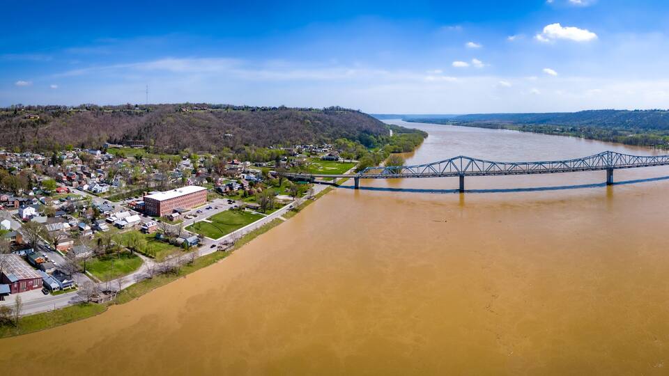 A river with a bridge spanning across it, surrounded by a town and hills.