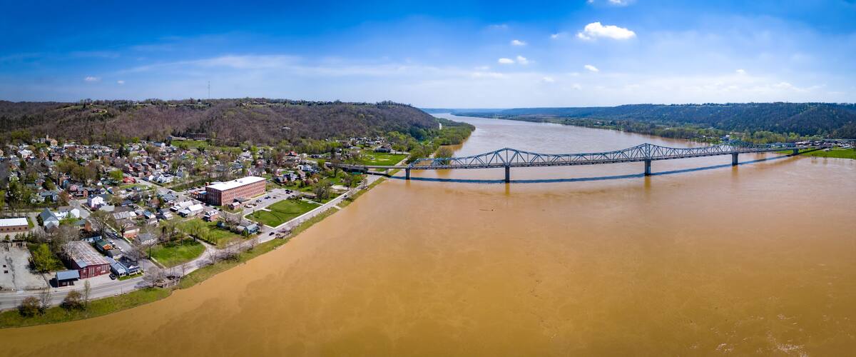 A river with a bridge spanning across it, surrounded by a town and hills.