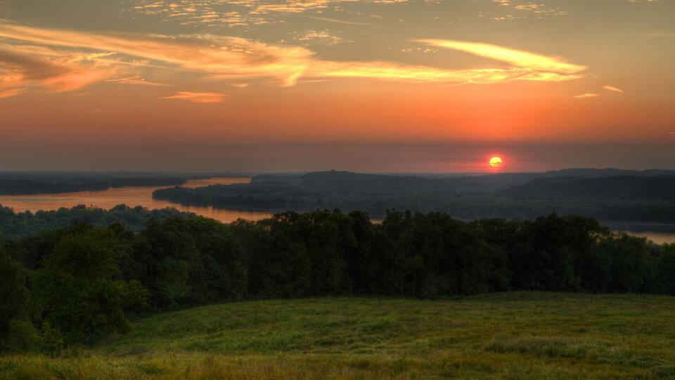 A sunset over a lake surrounded by hills and dense forests.