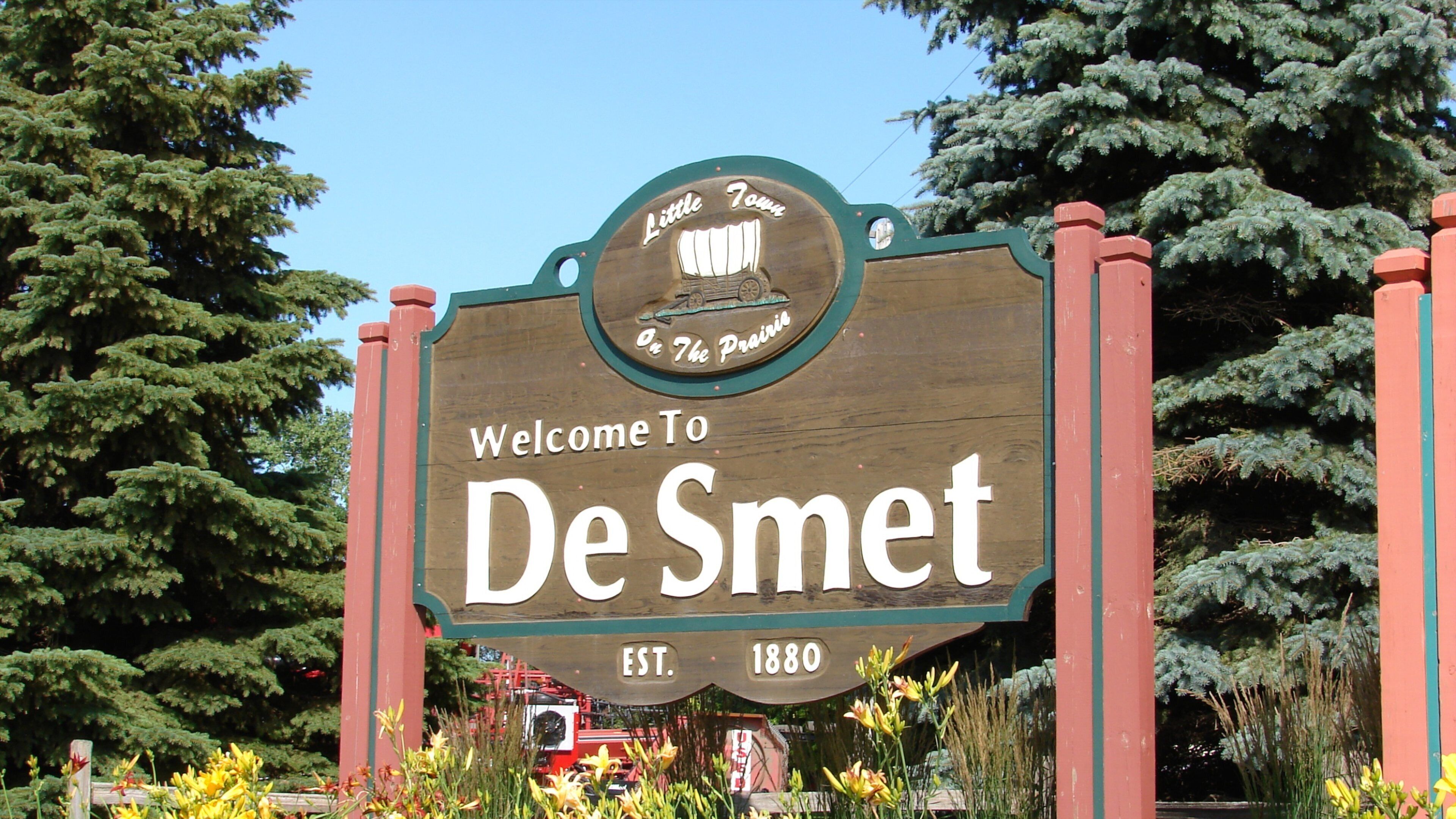 A wooden welcome sign for De Smet, established in 1880, with a logo of a covered wagon and a prairie scene.