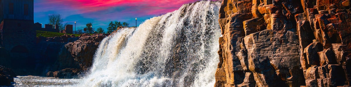 A waterfall cascading over rocky terrain with a sunset sky.