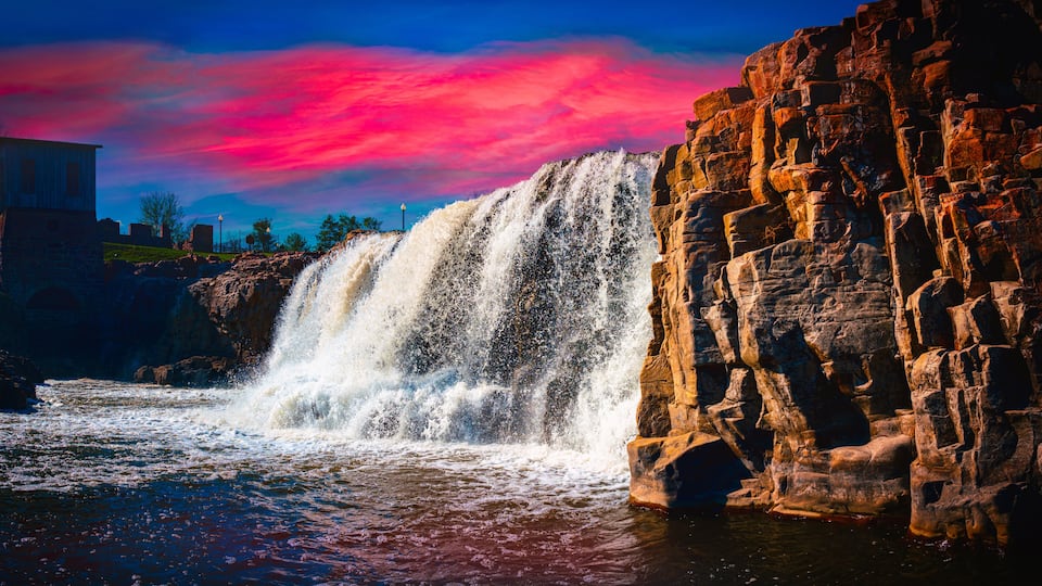 A waterfall cascading over rocky terrain with a sunset sky.