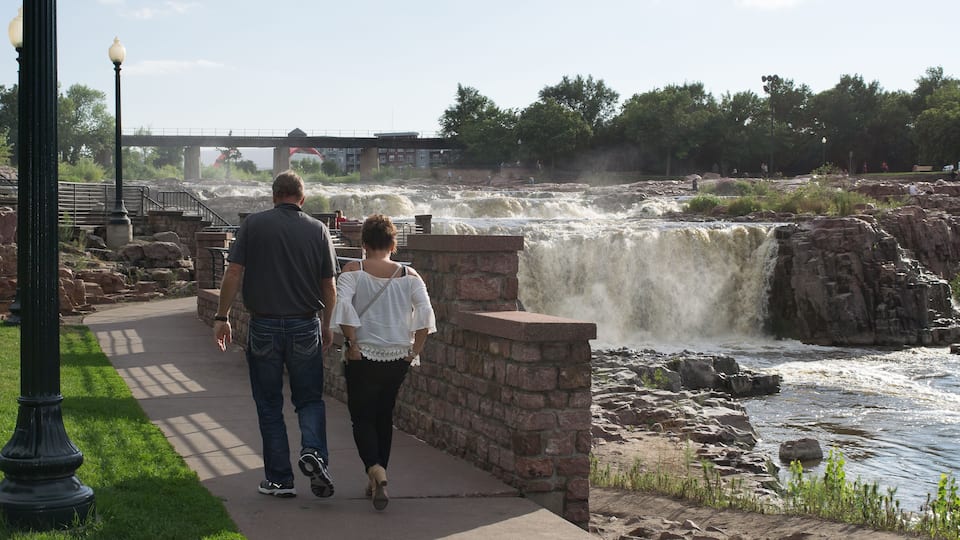 A man and woman walking along a concrete path beside a waterfall.