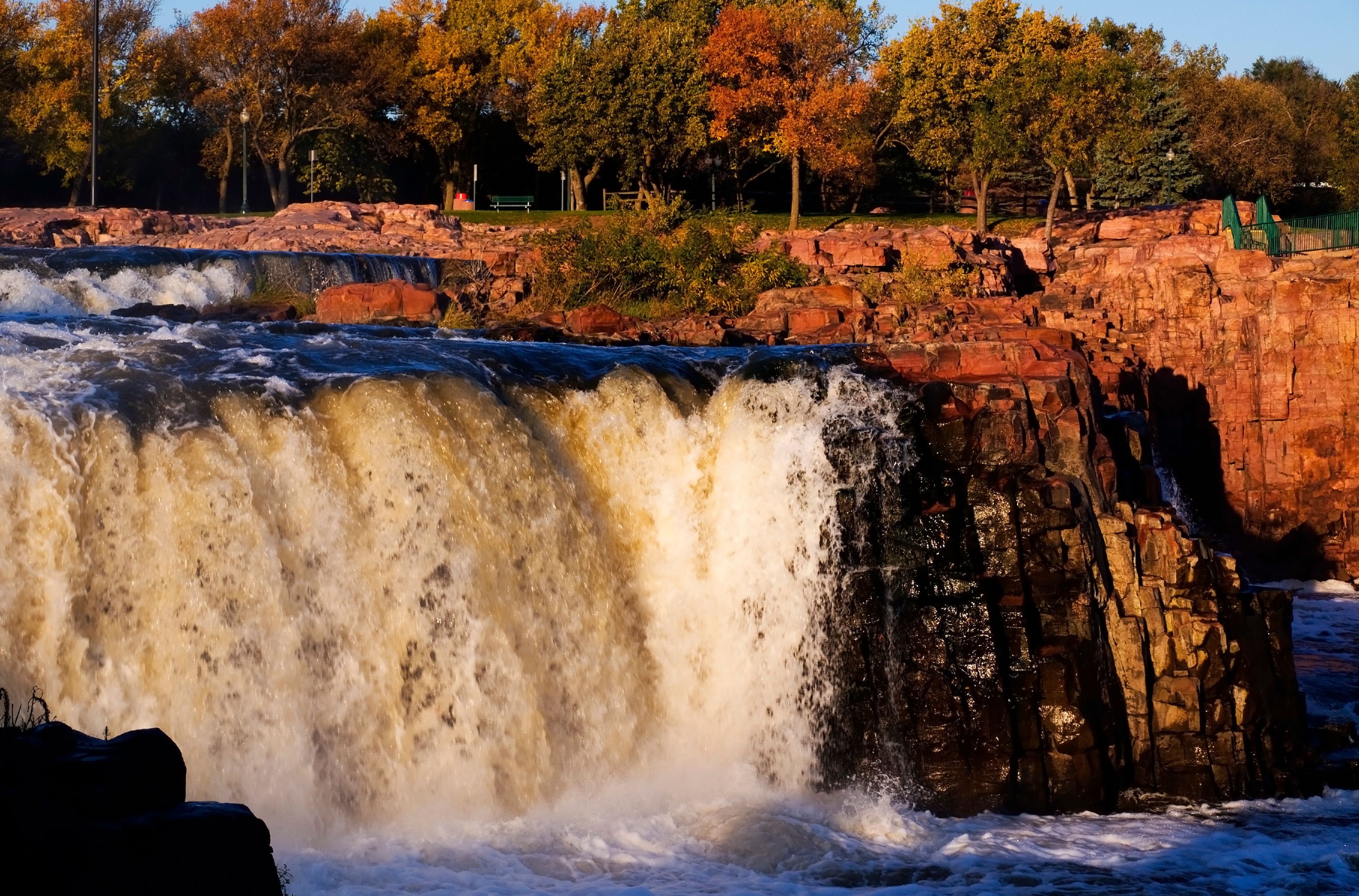 A waterfall cascading over rocky terrain with autumn foliage in the background.