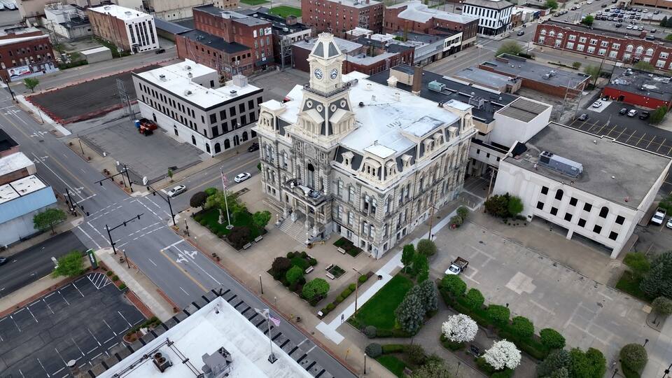 An aerial view of a historic building with a clock tower, surrounded by streets and other buildings.