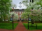 A brick building with a clock tower, surrounded by blooming trees and a brick pathway.