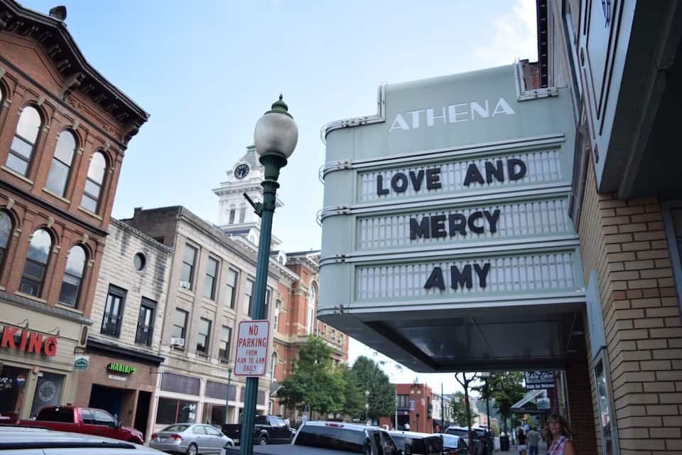 Un théâtre dont la façade porte l’inscription « ATHENA LOVE AND MERCY AMY », avec un panneau « INTERDIT DE STATIONNER » et une tour de l’horloge en arrière-plan.