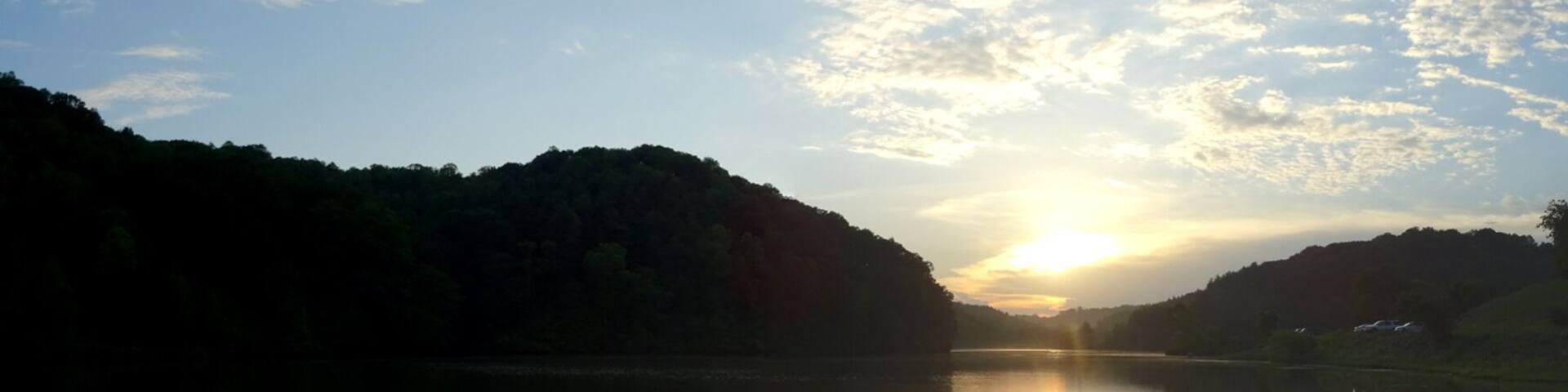 A calm lake reflecting the sky and surrounding hills during sunrise or sunset.