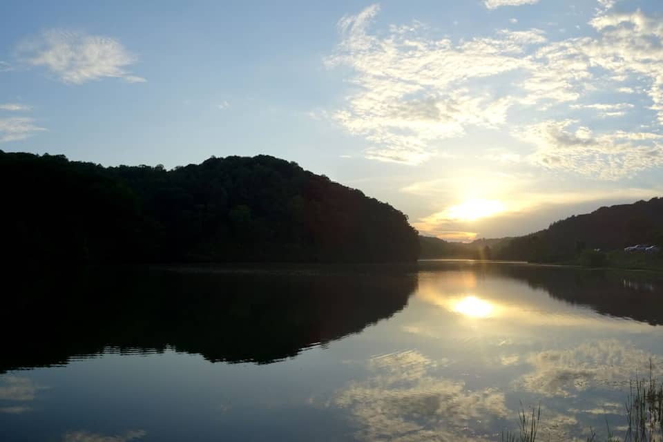 A calm lake reflecting the sky and surrounding hills during sunrise or sunset.