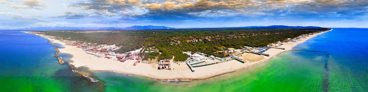 Luftaufnahme einer Küstenstadt mit Strand, Gebäuden und einem bewaldeten Gebiet.