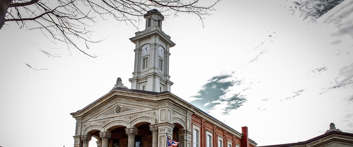 A historic building with a clock tower, columns, and a flag.