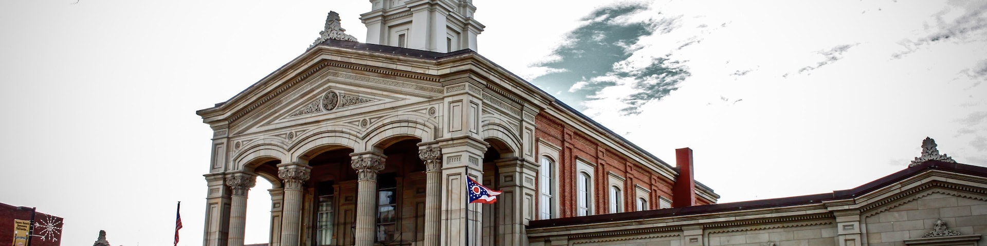 A historic building with a clock tower, columns, and a flag.