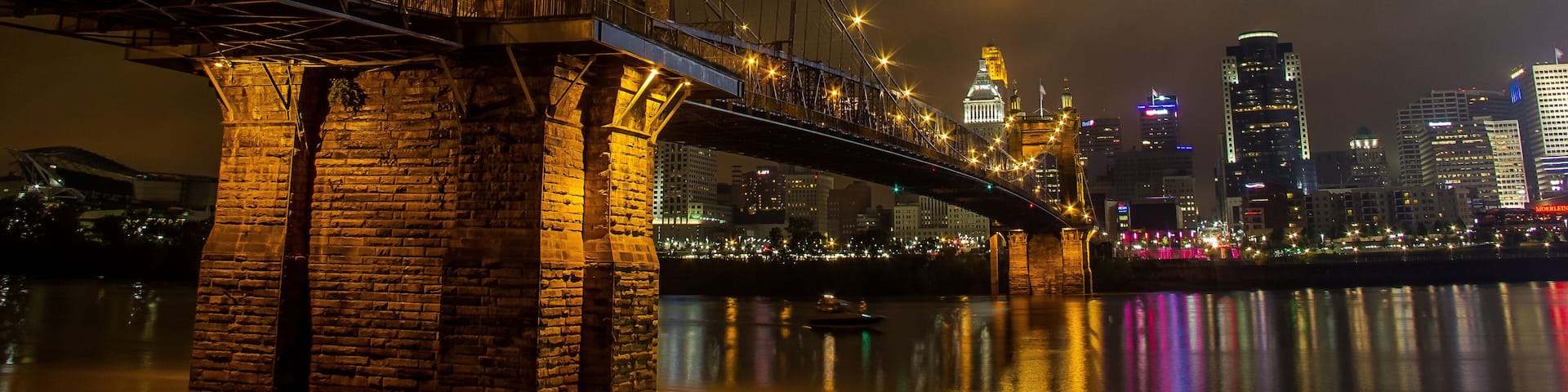 A lit bridge with a historic arch and modern buildings in the background.