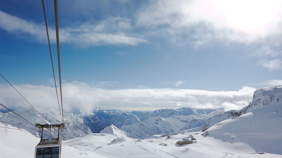 A cable car moving over a snowy mountain landscape with clear skies and distant peaks.