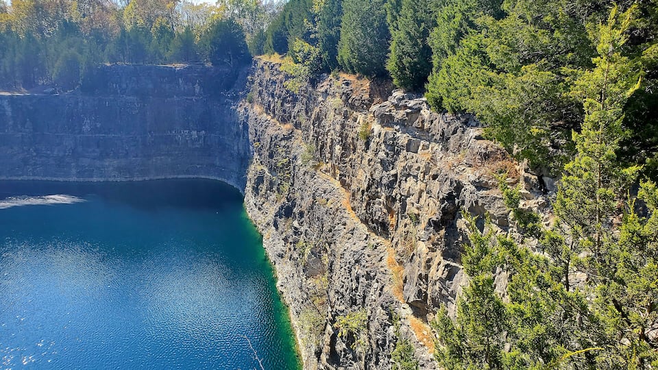 A rocky cliff with a deep blue body of water at its base.