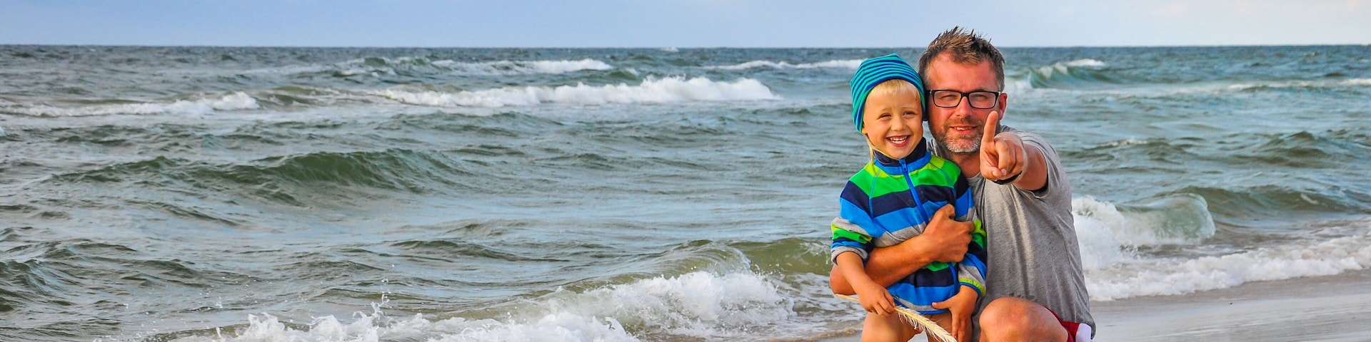 A beach with waves, a person holding a child, and a clear sky.