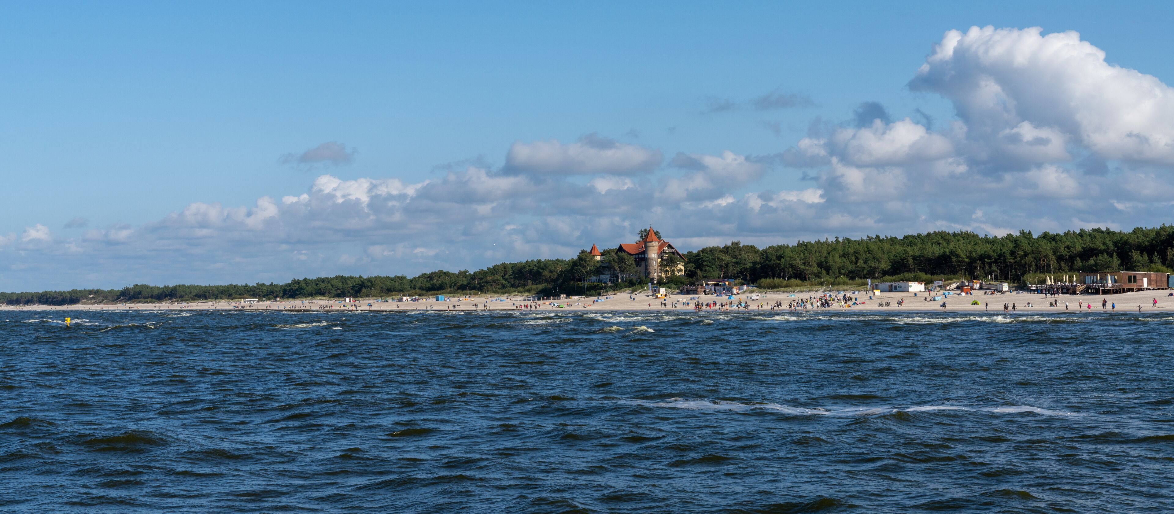 A beach with waves, a forest, and a tower.
