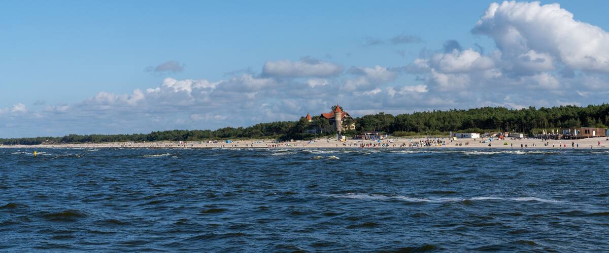 A beach with waves, a forest, and a tower.