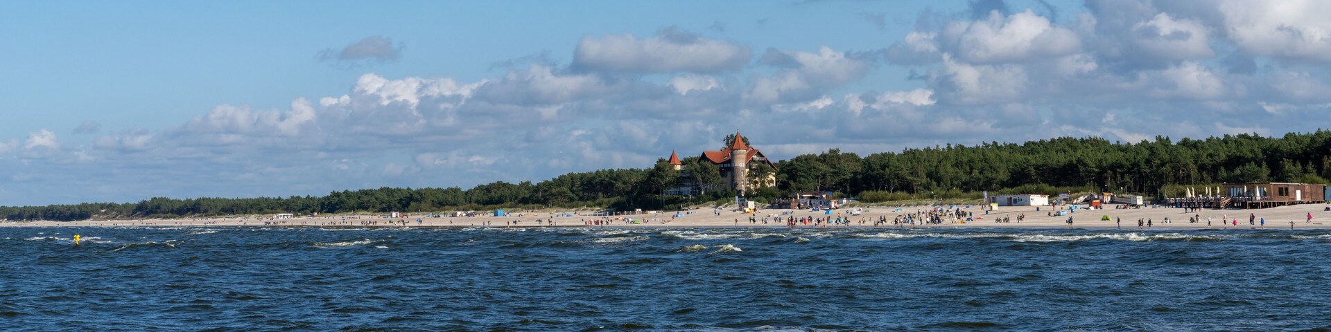 A beach with waves, a forest, and a tower.