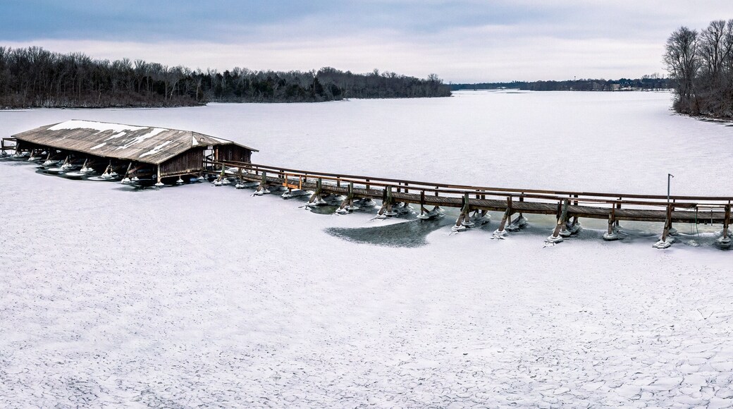 An icy dock with an old walking bridge sits on top of an snowy lake.