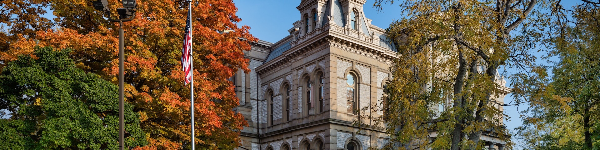 A historic building with a clock tower, surrounded by autumn-colored trees and American flags.