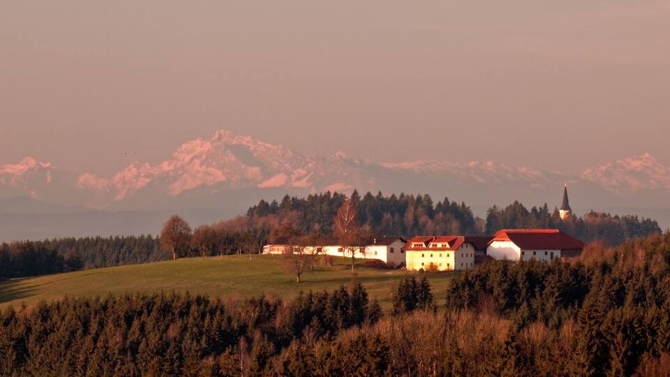 A rural landscape with a church, houses, and a mountain range in the background.