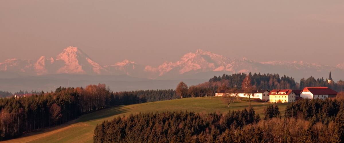 A rural landscape with a church, houses, and a mountain range in the background.