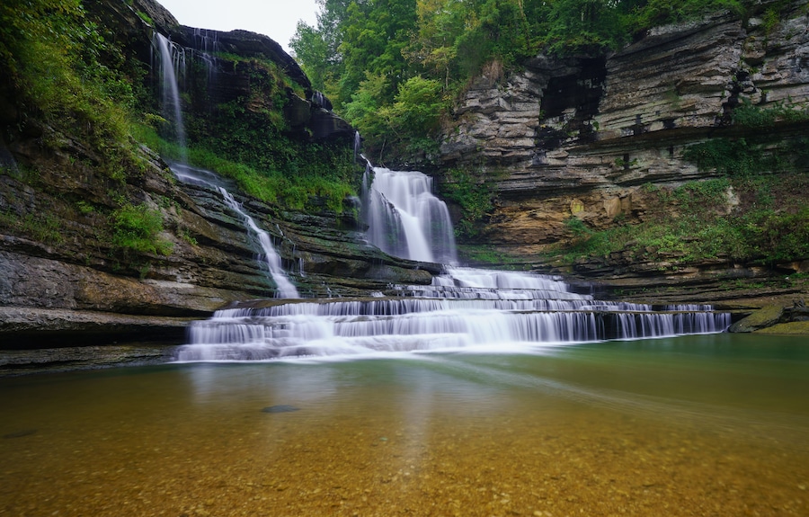 Una cascada escalonada que se precipita en una piscina cristalina, rodeada de riscos y exuberante vegetación.