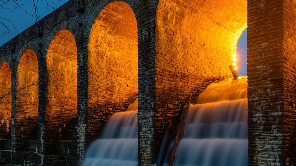 A stone bridge with multiple arches and a waterfall flowing through it.
