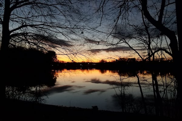 A sunset over a calm lake with silhouetted trees and a clear sky.