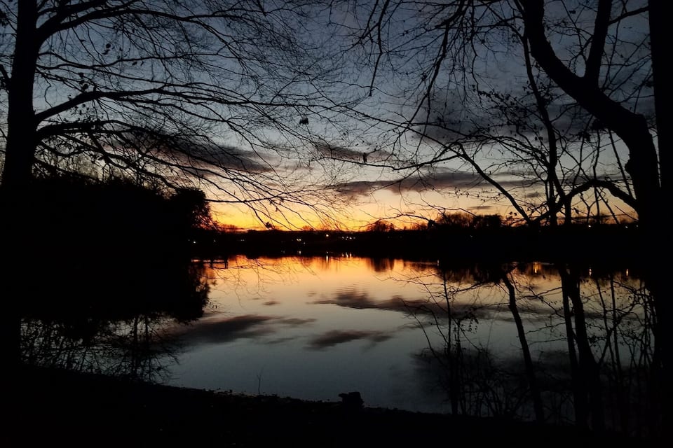 Un atardecer sobre un lago tranquilo con siluetas de árboles y un cielo despejado.