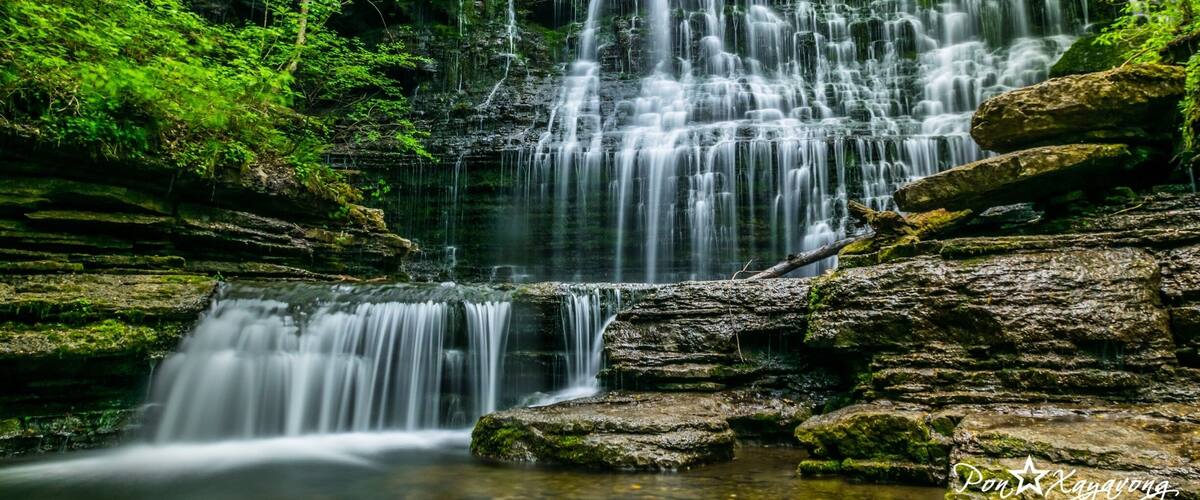 A multi-tiered waterfall surrounded by lush green foliage.