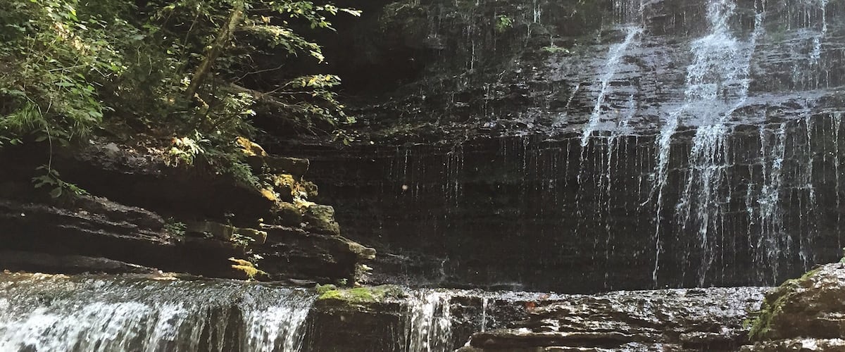 A waterfall cascading over rocky terrain surrounded by dense foliage.