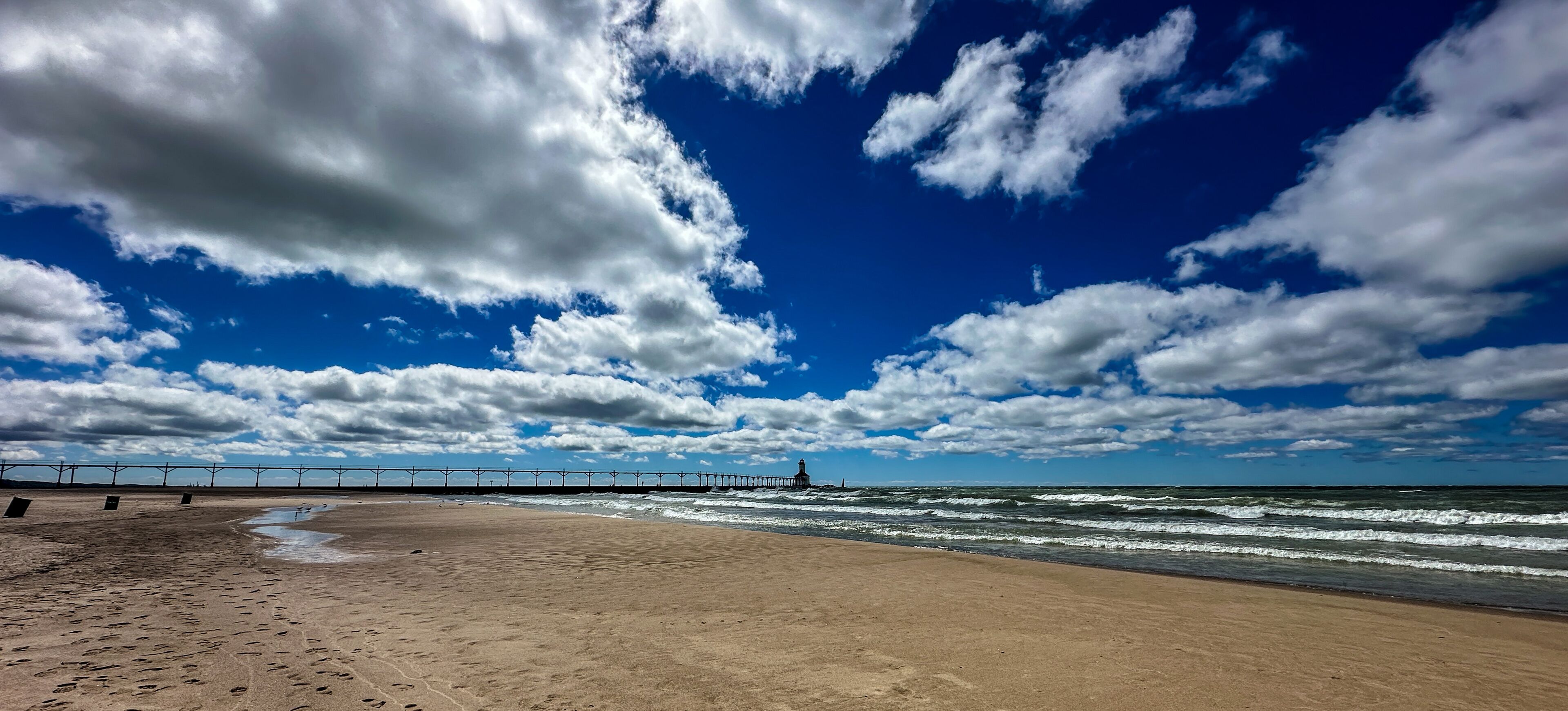 A beach with footprints, waves, a pier, and a lighthouse.