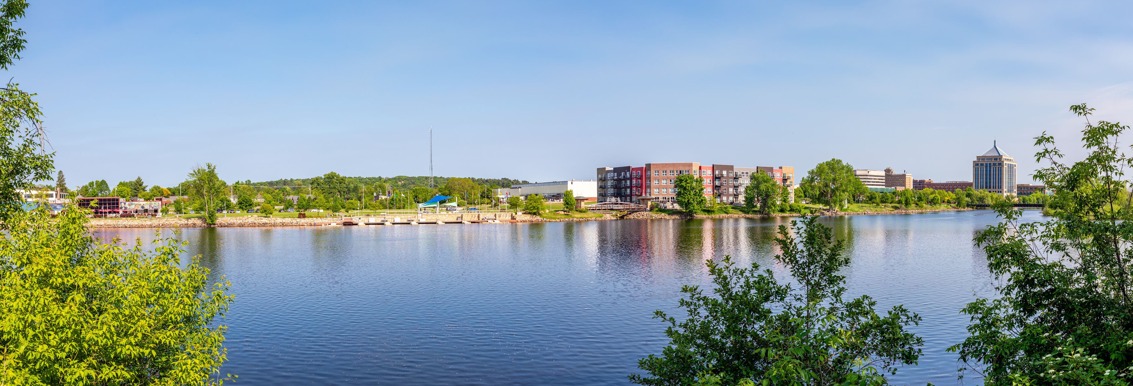 A calm lake with a bridge, buildings, and greenery.