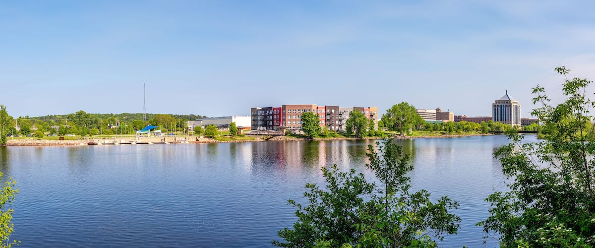 A calm lake with a bridge, buildings, and greenery.