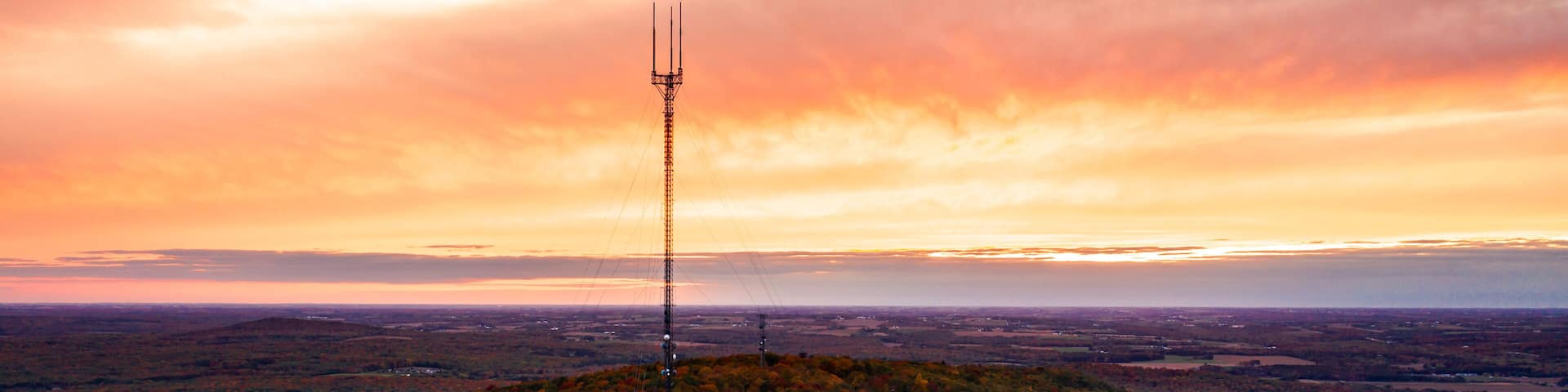 Beautiful aerial drone photograph of rib mountain as the sky erupts with orange and pink colored clouds beyond the broadcast tower at sunset with colorful fall leaves or autumn foliage on hill below.
