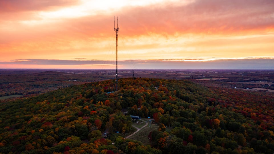 A telecommunications tower on a hilltop surrounded by autumn-colored trees.