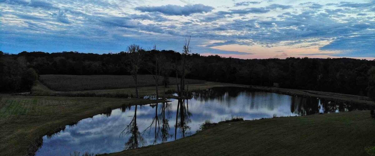 A calm lake reflecting the sky, surrounded by grassy fields and trees.