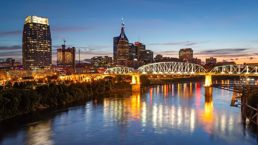 Une vue sur les gratte-ciel d’une ville au crépuscule, avec un pont imposant enjambant une rivière.