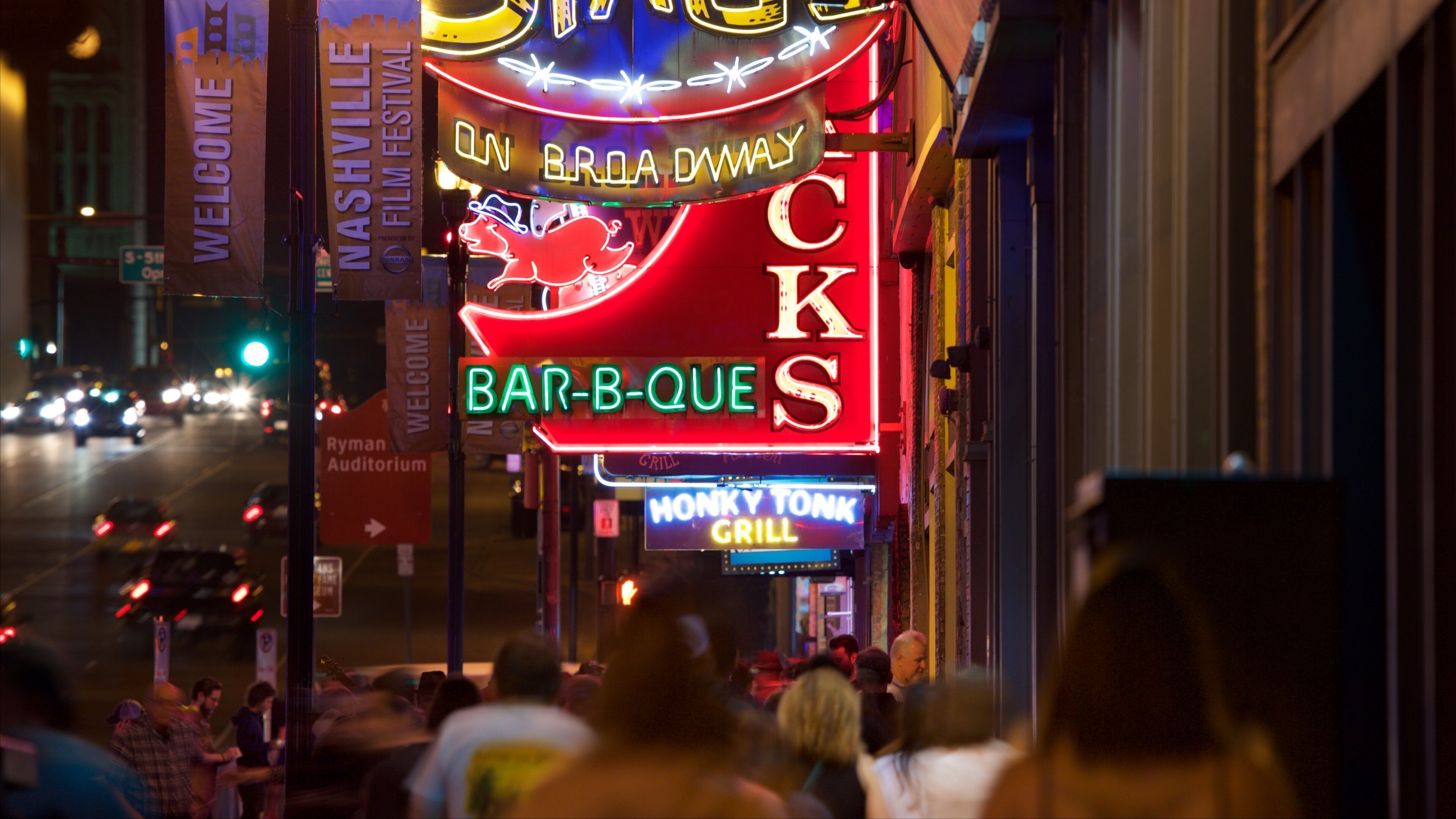 En neonskilte for 'Bar-B-Que' og 'Monkey Tonk Grill' på en travl gade om natten.